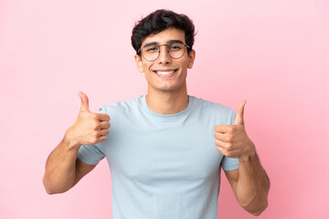 Young Argentinian man isolated on pink background With glasses and with thumb up