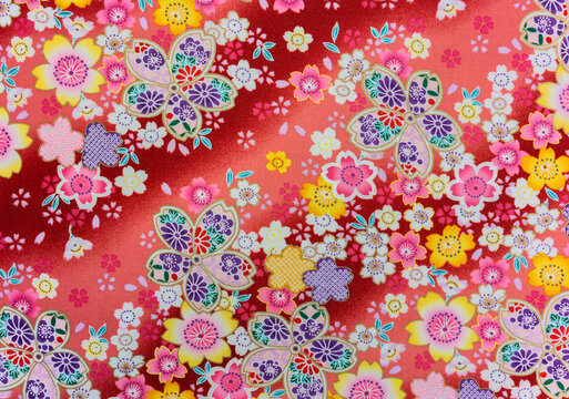 Close up on a high detailed photograph of a Japanese pattern design illustrated with colorful flowers enhanced with golden color printed on a furoshiki cloth made in cotton fabric on a red background.