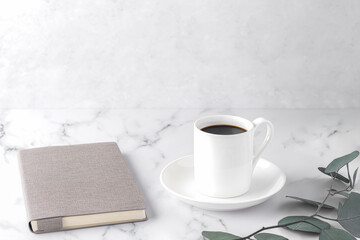Cozy morning, with cup of coffee, notebook, eucalyptus twigs, on a white marble table. Scandinavian style, lagom. Balanced lifestyle concept. Horizontal, copy space.