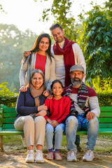 Fototapeta premium happy Indian family sitting at park in winter wear or warm clothes