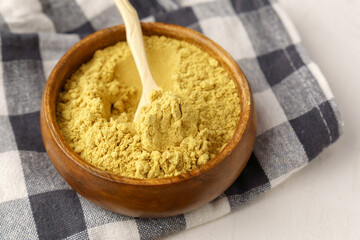 Mustard powder close up in a bowl on white table, selective focus.