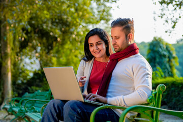 Fototapeta na wymiar Young indian couple using laptop at park.