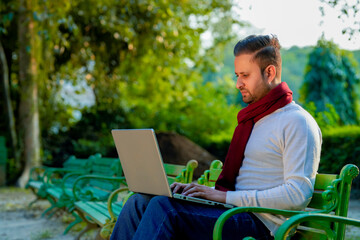 Young indian man in warm wear and working on laptop at park