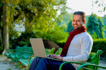 Young indian man in warm wear and working on laptop at park