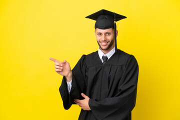 Young university graduate caucasian man isolated on yellow background pointing finger to the side