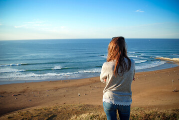 Young girl looks out ocean from the coast above sopelana beach. Spain