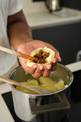 Close up of cuban woman hands filling mashed potatoes with minced beef to prepare cuban style stuffed potatoes.