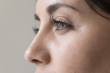 Brown eyes close up of young beautiful black haired woman with healthy smooth skin looking away. Side view, cropped shot. Female model promoting beauty care, cosmetology.