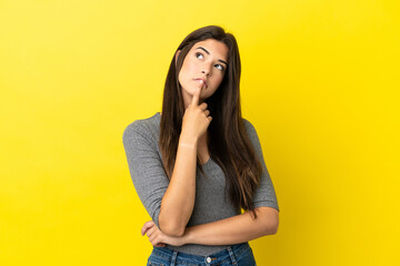 Young Brazilian woman isolated on yellow background having doubts while looking up