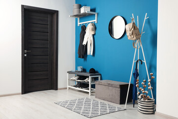 Stylish hallway with coat rack and shoe storage bench near blue wall. Interior design