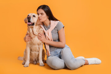 Happy woman kissing cute Labrador Retriever on orange background