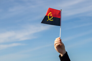 Angolan flag in hand flutters in the wind against the sky, independence national day of Angola,...