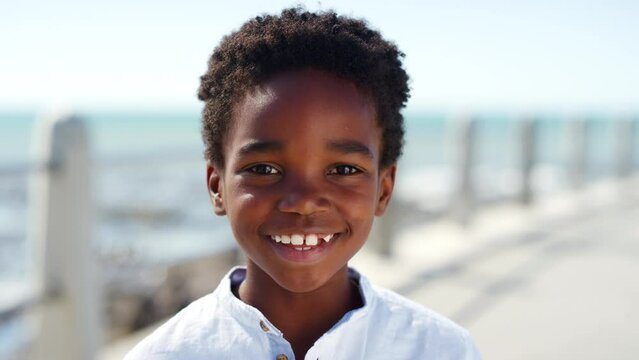 Face, happy and smile of kid at beach on vacation, holiday or summer trip. Relax, freedom and portrait of black boy from South Africa smiling, having fun and enjoying time by seashore or promenade.