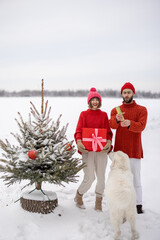 Man and woman have fun together, shooting confetti near Christmas tree outdoors. Young couple...