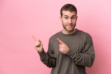 Young caucasian man isolated on pink background frightened and pointing to the side