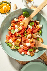 Classic italian panzanell salad with tomatoes, basil, bread, mozzarella on white kitchen table. Served with wine. Overhead view.