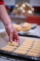 Nahaufnahme von Hände einer Frau, die mit einen alten Drehwolf, Spritzgebäck Plätzchen zu Weihnachten backt. Im Hintergrund das Bokeh von Weihnachtsbeleuchtung