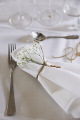 Wedding. Decor. Banquet. A table with a white tablecloth in the festive hall is decorated with a composition of flowers and greenery, there are candles, glasses, cutlery and name plates for guests