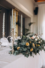 Wedding. Decor. The festive table is decorated with a composition of flowers and greenery. There are plates, glasses and candlesticks on the table