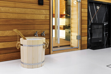 Finnish bathroom with a small wooden sauna and firewood stove. Modern spa interior with a glass door and wooden walls
