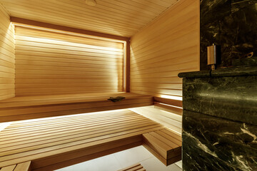 Finnish bathroom with a small wooden sauna and firewood stove. Modern spa interior with a glass door and wooden walls