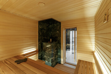 Finnish bathroom with a small wooden sauna and firewood stove. Modern spa interior with a glass door and wooden walls