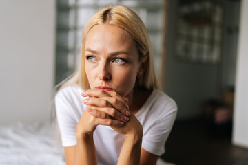Closeup face of thoughtful woman sitting alone at home and looking away with sad expression holding...