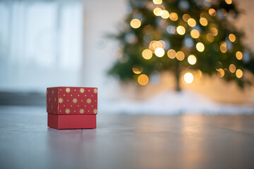 Weihnachtlicher Hintergrund mit Platzhalter. Geschenk vor einen beleuchteten Weihnachtsbaum.