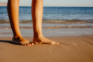 Beach feet close up - barefoot woman walking in ocean water waves. Female young adult legs and toes wearing an ankle bracelet anklet relaxing in summer vacation travel. feet on the beach.
