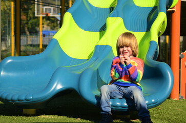 Cute boy in a colorful sweater on the playground. The child laughs, plays, rides down the slide....