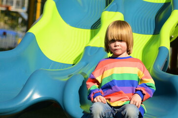 Cute boy in a colorful sweater on the playground. The child laughs, plays, rides down the slide. Concept: children's holidays, amusement park, holidays, family vacation, kindergarten.