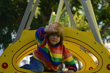 Positive boy in a colorful sweater on the playground. The child laughs, plays, rides down the...