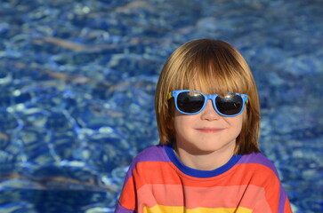 Positive little boy in sunglasses and a multi-colored jacket on the background of the water. Space...
