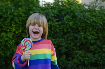 Boy 3 years old in a bright jacket on a background of green grass. Portrait of a cheerful child, good mood. The boy is holding a big caramel on a stick. Children and sweets, candies.