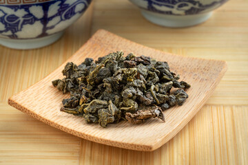 Fototapeta na wymiar Bamboo plate with Chinese Ti Kuan Yin organic oolong tea dried tea leaves close up 
