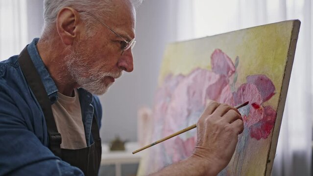 Close-up Caucasian senior man, talented painter enjoys his hobby at retirement - painting on canvas