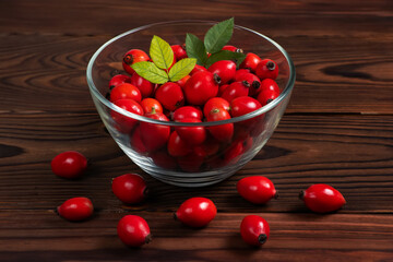 Fresh red Rose Hips in the glass bowl on wooden background, fresh Berries from the dog rose