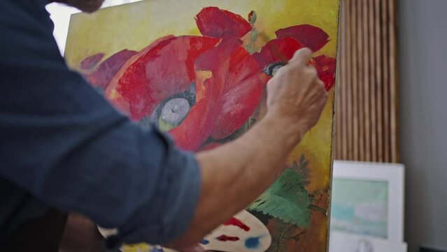 Male painter's hand with paintbrush applying red oil paint on canvas while drawing beautiful artwork