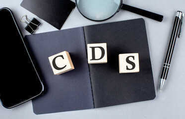 Word CDS on wooden block on black notebook with smartpone, credit card and magnifier