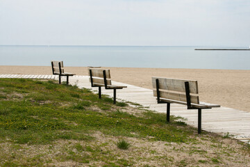 Three benches overlooking a sandy beach and the water on a gloomy, cloudy, overcast day.  Image has copy space.