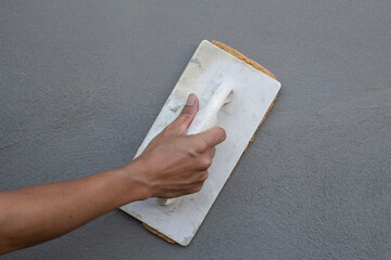 Hand of construction worker holding plastering trowel and sponge for using to smooth the walls in construction house site. - obrazy, fototapety, plakaty
