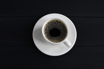 Coffee with foam standing on a saucer. Black wooden background, top view. Free space for text