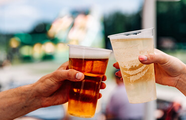 two plastick cup of beer in man and woman hands. Beer clinking outdoor
