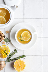 Ginger tea with lemon and rosemary in a white cup on a white background, a teapot and a sugar bowl...