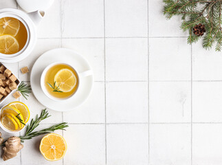 Ginger tea with lemon and rosemary in a white cup on a white background, a teapot and a sugar bowl with brown sugar stand nearby
