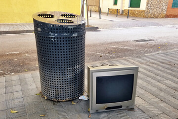 Broken old crt tv near a metal trash can on city street.