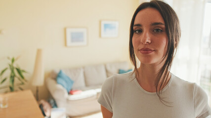 Close up, young beautiful woman crossing her arms and smiling at camera while standing at home