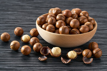Macadamia in wooden bowl on black table.