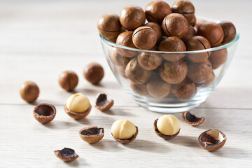 organic macadamia  in a glass plate and scattered on a white kitchen table, selective focus.