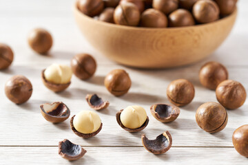 macadamia spill out of a wooden bowl on a white table, selective focus.